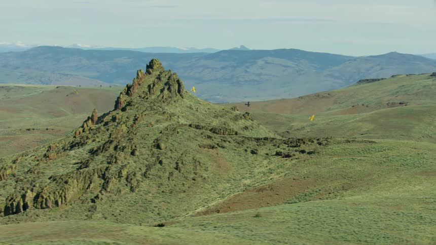 A group of airplanes fly over a large cone shaped rock formation deep in the desert