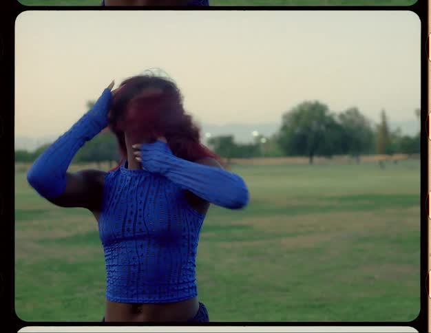 Woman with red hair blue top and sports pants dances on lawn in public park