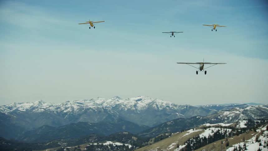 Four small backcountry propeller airplanes flying above snow capped mountain ridges and slopes in the wilds of Idaho