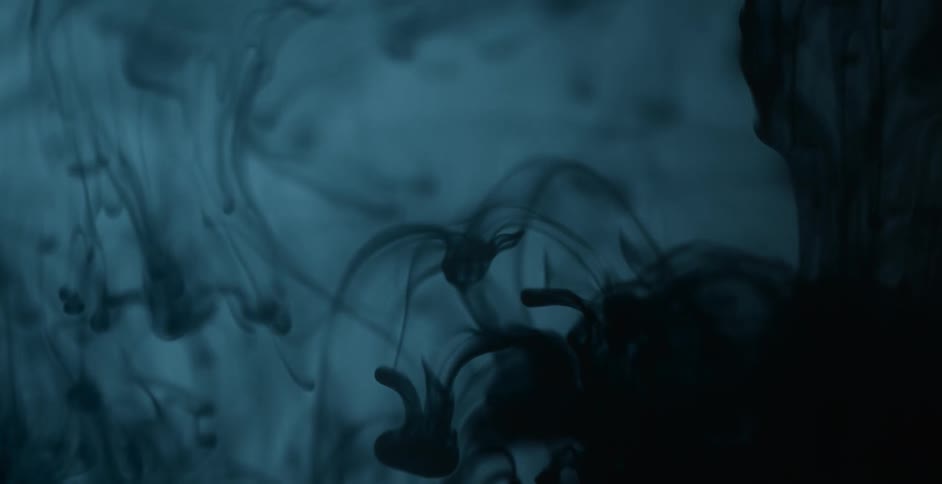 Dark dye sinks and falls in liquid as a light glows and fades