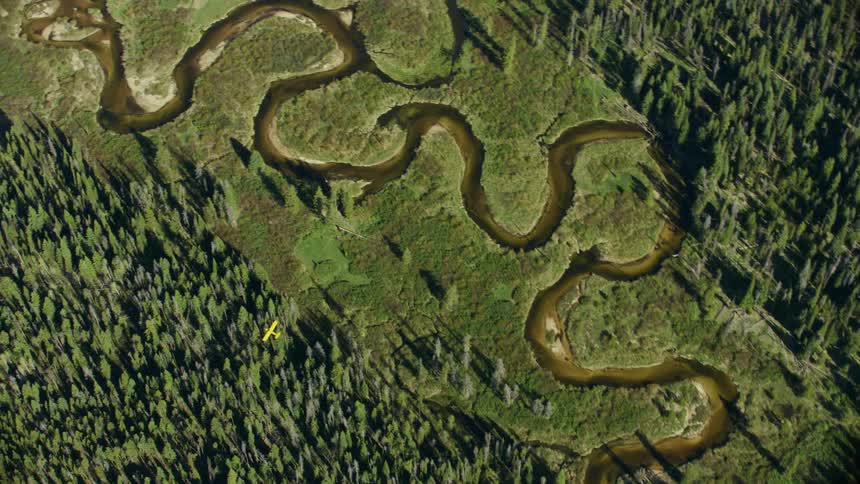 A yellow Carbon Piper Cub flies over a meandering river in the high altitude Idaho Backcountry