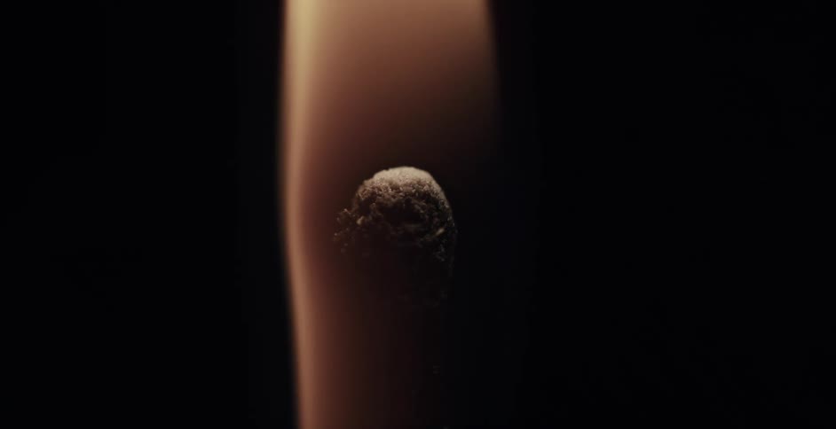 A wooden match ignites and a flame burns brightly in the darkness