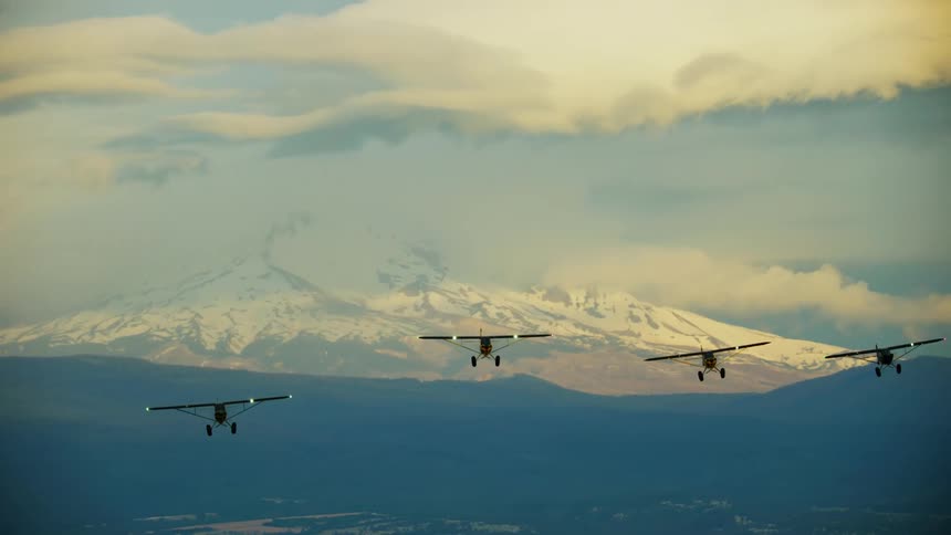 Group of backcountry airplanes fly in formation with the beauty of the Oregon Cascade Mountains in the background at sunrise