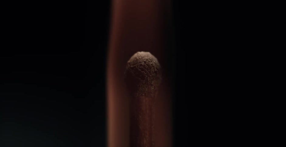 A wooden match ignites and a flame burns brightly in the darkness