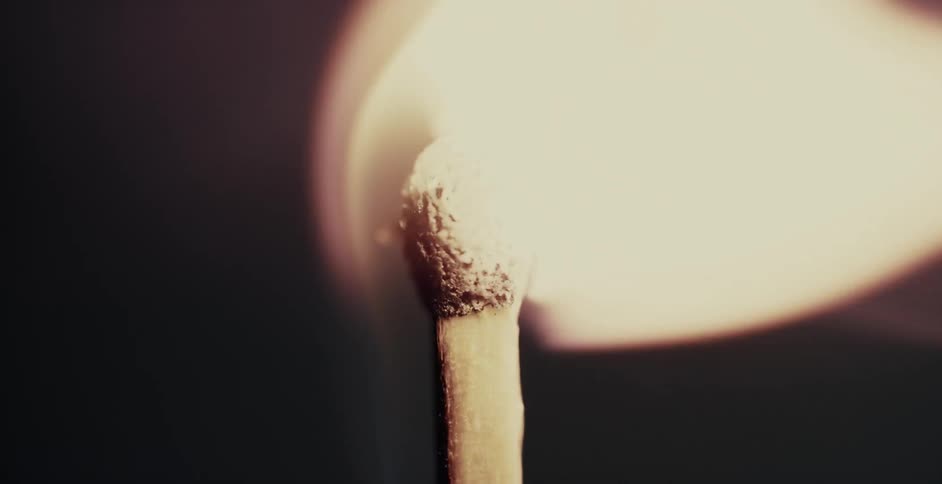 A flame ignites a wooden match and it burns brightly in the darkness