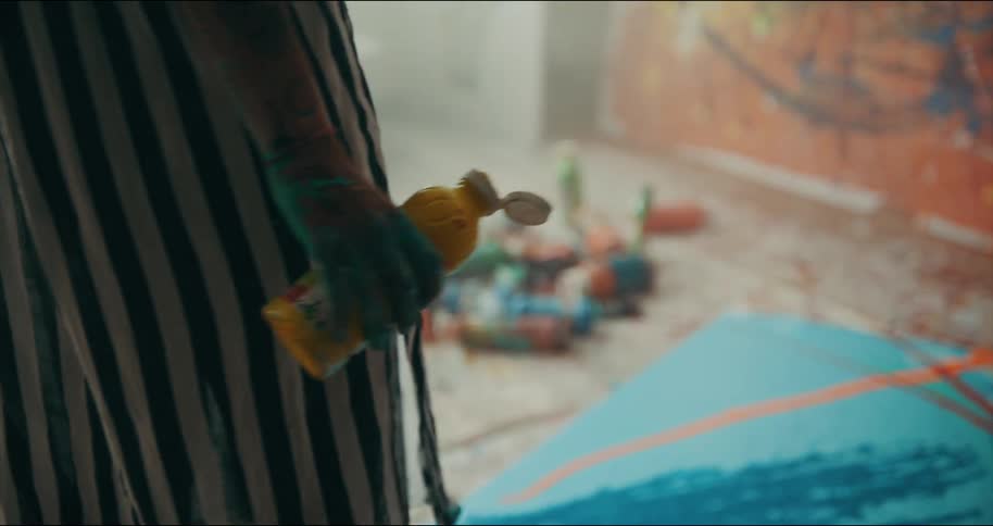 A woman stands holding a squeeze bottle of paint swaying back and forth over her canvas