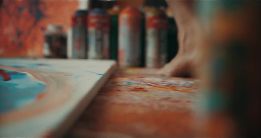 A woman tiptoes to get around a canvas and dozens of spray paint canisters on her floor