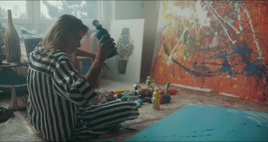 Female artist splashes paint across canvas lying on studio floor using a paint bottle