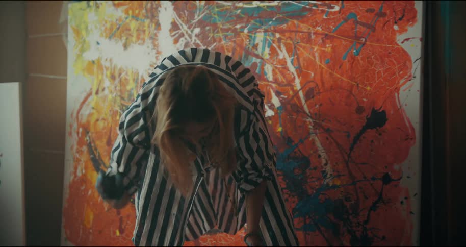 Woman wearing a striped garment bends over in front of a canvas and shakes her hands towards the floor