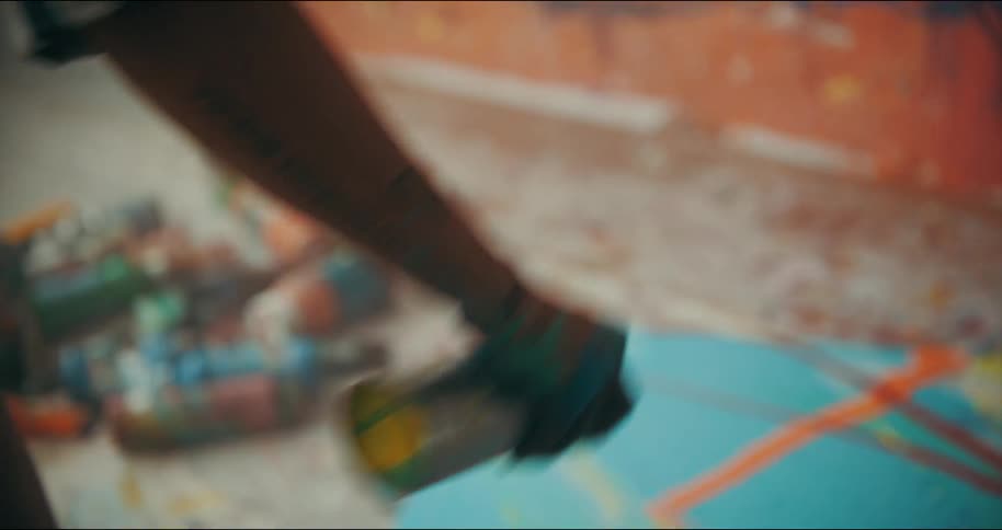 Artis shakes a can of spray paint over an oil painting laying in the floor