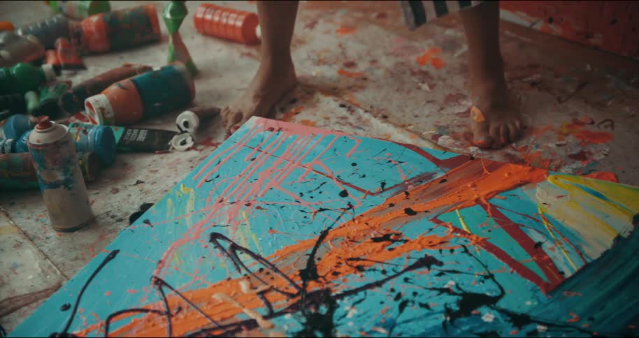 Artist wearing a striped garment shakes a tube of paint and splashes the paint onto a canvas