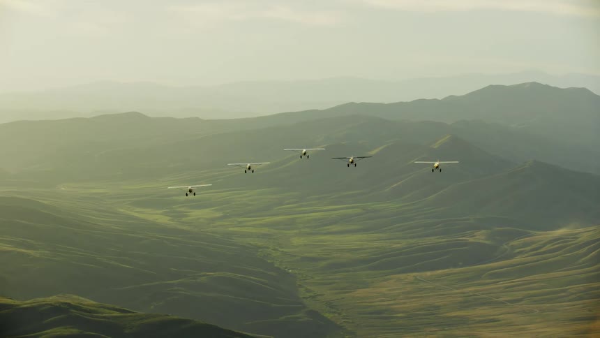 Five backcountry airplanes with fixed landing gear fly over mist valley in mountainous terrain