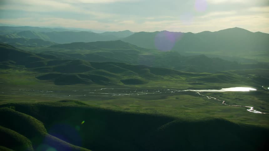 Aerial view of a web of small rivers flowing over the green lush landscape next to the mountains at morning