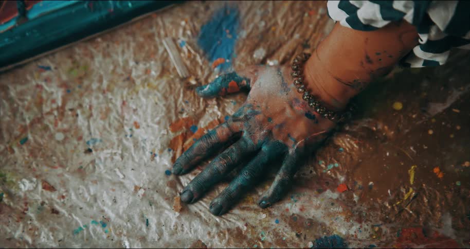 An artists fingers covered in paint resting on a plastic sheet