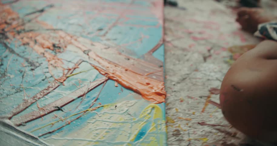 Woman wearing a striped shirt sits on the floor and looks at a painting laying in front of her