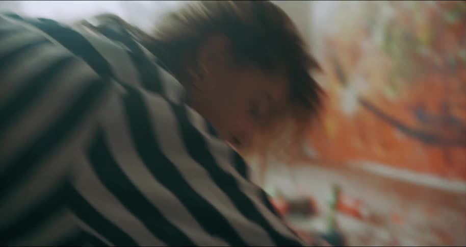 Woman wearing a striped shirt kneels on the floor and paints on a canvas with a can of spray paint