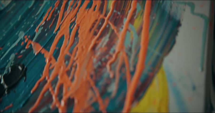 Woman wearing a striped garment squeezes orange paint from a tube onto a canvas and the paint runs down the canvas