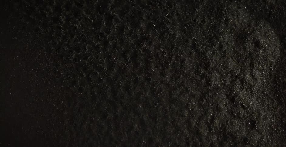 Gray grit particles flow and form pits and pockets as they vibrate
