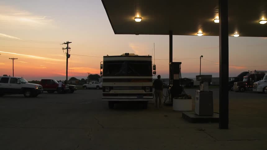 Person fueling a camper truck at gas station at dusk