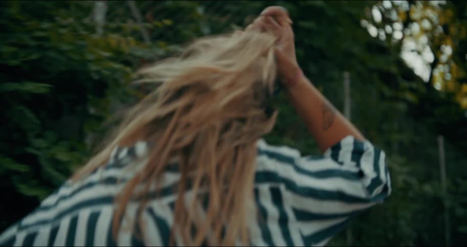 Blonde woman wearing a striped shirt walks past a tree lined hill on a sunny day