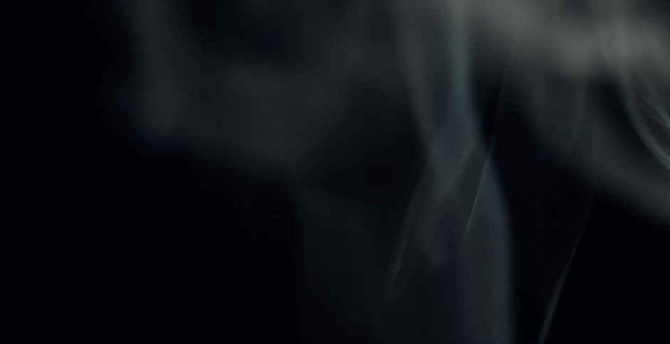 Gray smoke rises up on black background