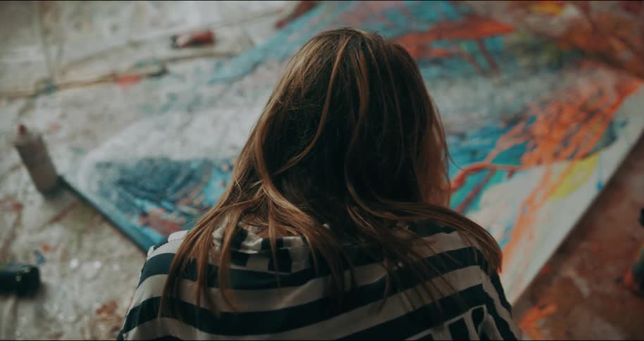 Woman moves her arms while crouching in front of a painted canvas