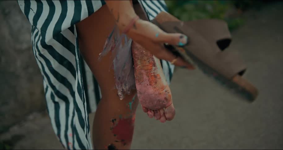 Young woman takes of her sandals to look at the paint stains on the sole of her feet