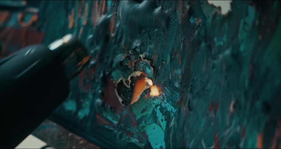 Someone is using a small torch to light a painting on fire