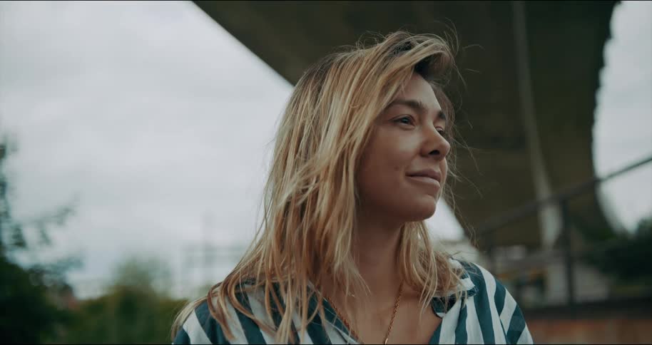 Close up of a young woman with blonde hair standing under a highway at daytime
