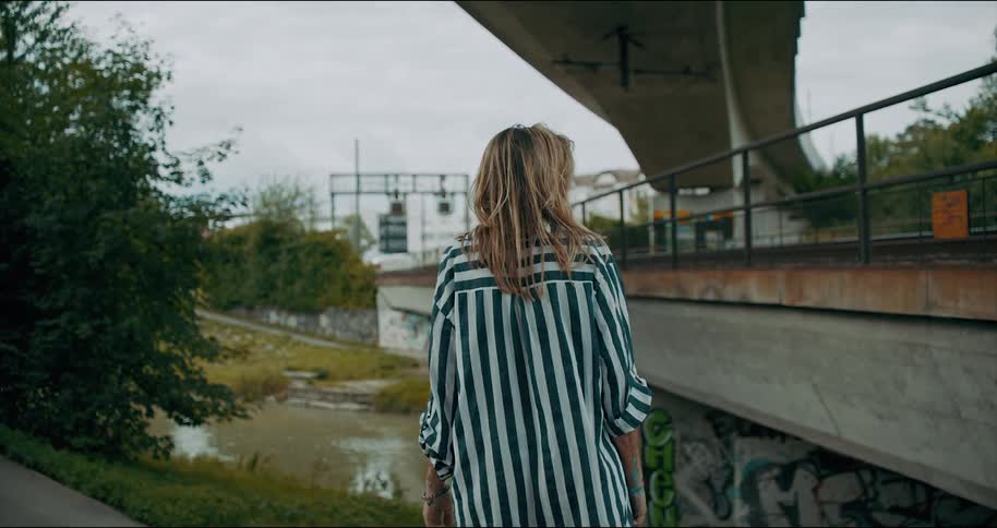 A woman standing on a riverbank looking at the pedestrian bridge and highway ramp