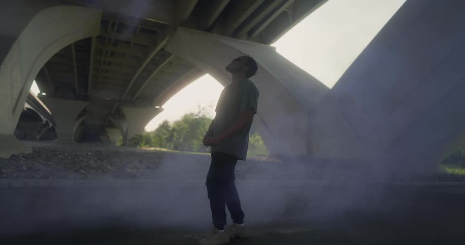 A man stands under a bridge as smoke surrounds him