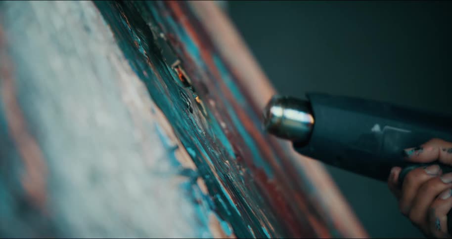A woman holding a heat gun is heating up paint on a canvas making the paint catch on fire