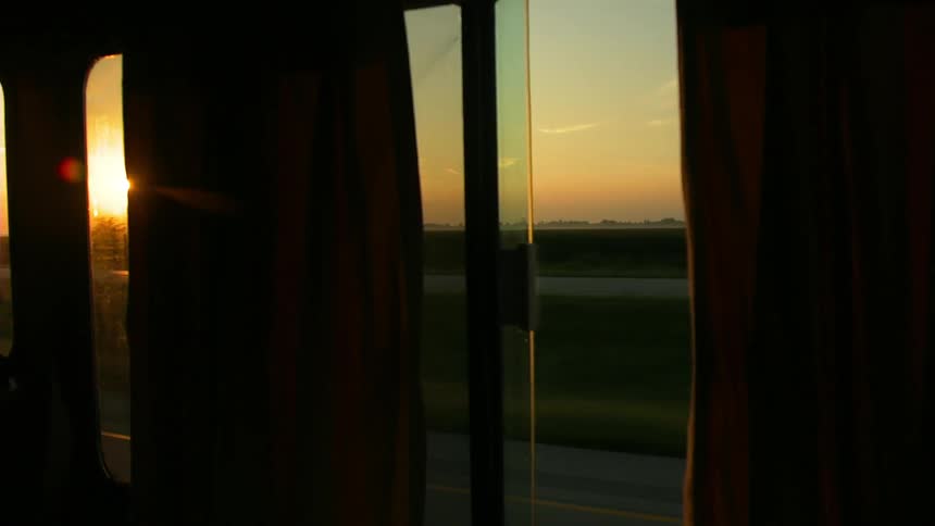 A vehicle drives on a rural road at sunset