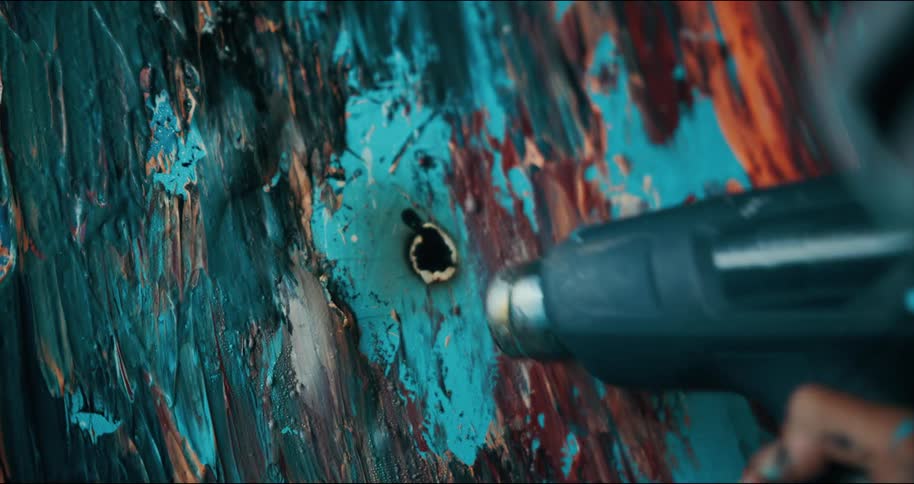 Artist burns parts of the canvas of a finished abstract modern painting and extinguish the flames with a hair dryer