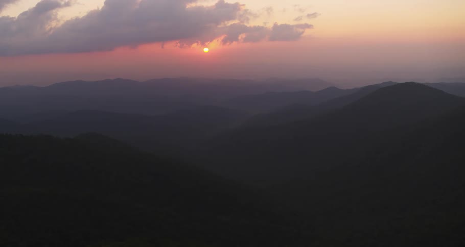 The sun sets over mountains in a hazy and cloudy red sky