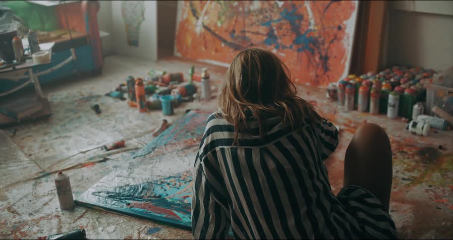 A woman pours a bottle of paint onto a canvas