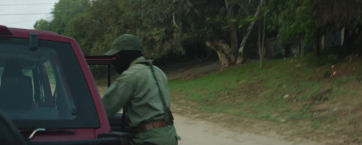 A man wearing military gear parks a car on a rural road and throws a hostage to the ground