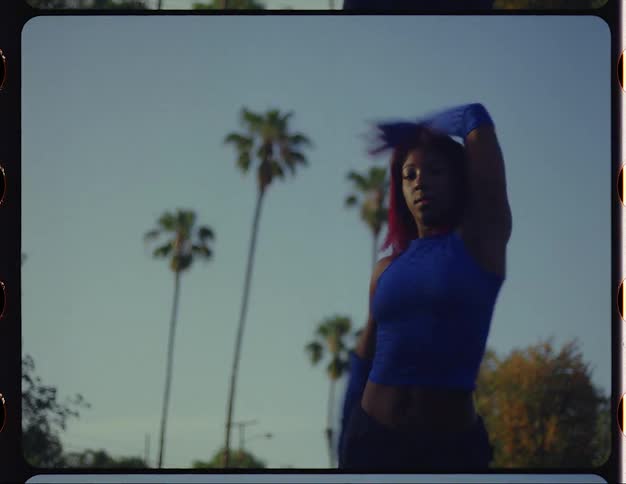 A woman performing dance steps and moves outside with palm trees behind her