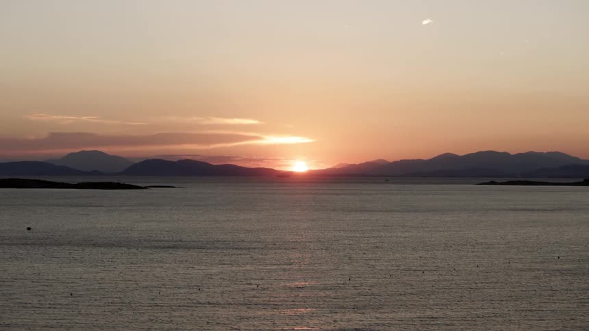 Sun sits on the horizon in a red sky shining ocean and turning mountains into silhouettes