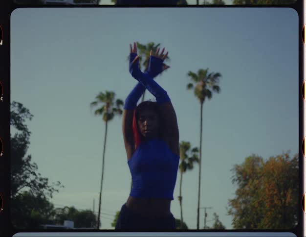 A woman dances in the middle of a road lined with palm trees