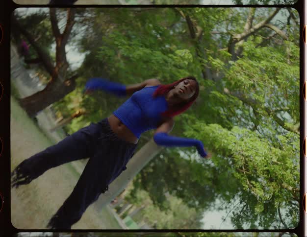 Twisting footage of a woman with red hair energetically dancing on a park caught on vintage film
