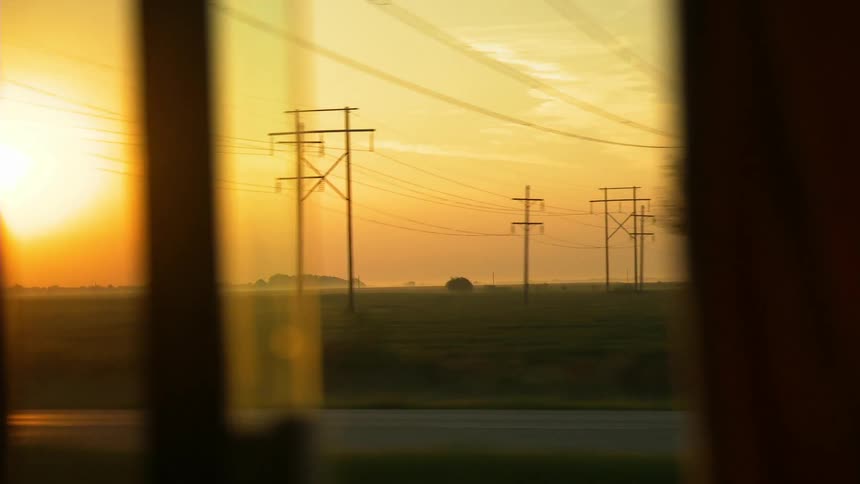 A vehicle is passing a large green field covered with electric poles at sunset