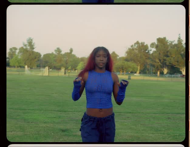 Woman with red hair blue top and sports pants dances on lawn in public park