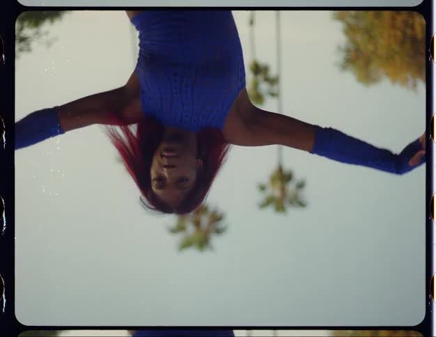 Woman with red hair blue top and sports pants dances on lawn in public park