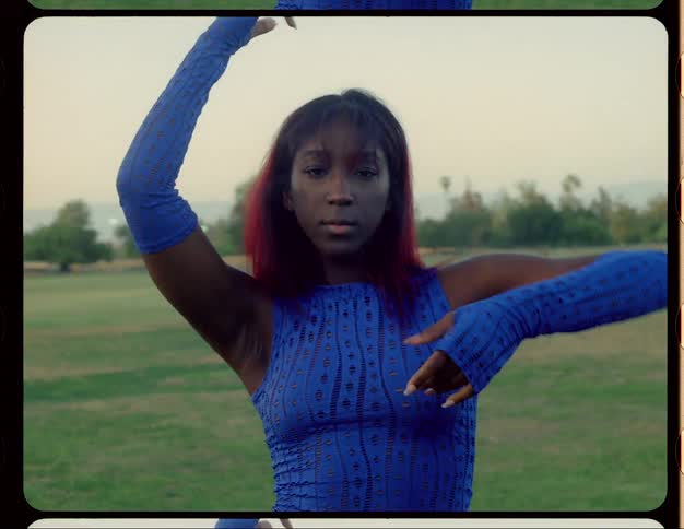 Female dancer with red hair blue top and sports pants dances on lawn in public park