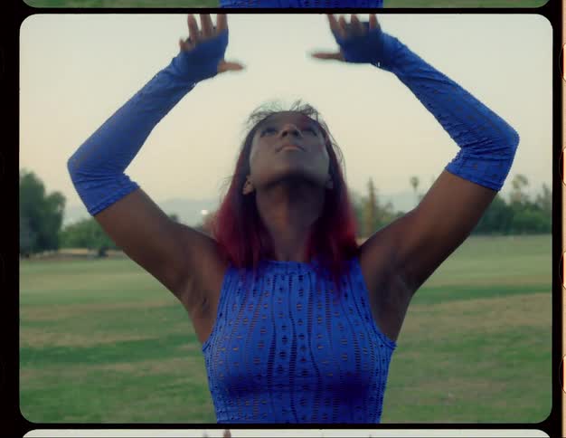 Woman with red hair blue top and sports pants dances on lawn in public park