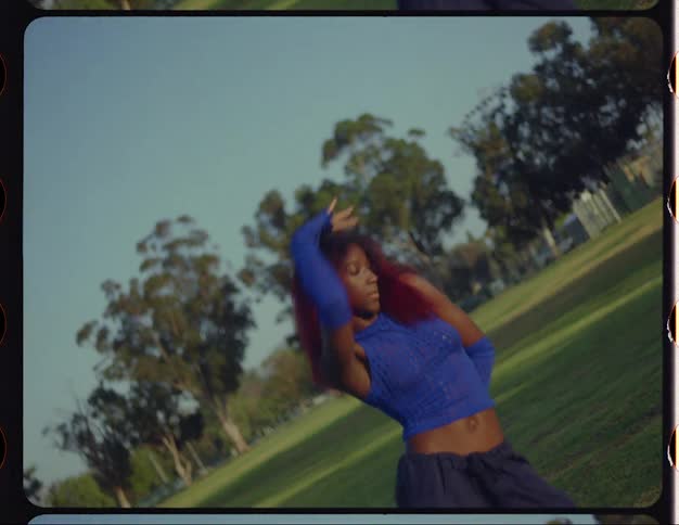 Young black woman dancing in the middle of the grass field in a public park on a sunny day