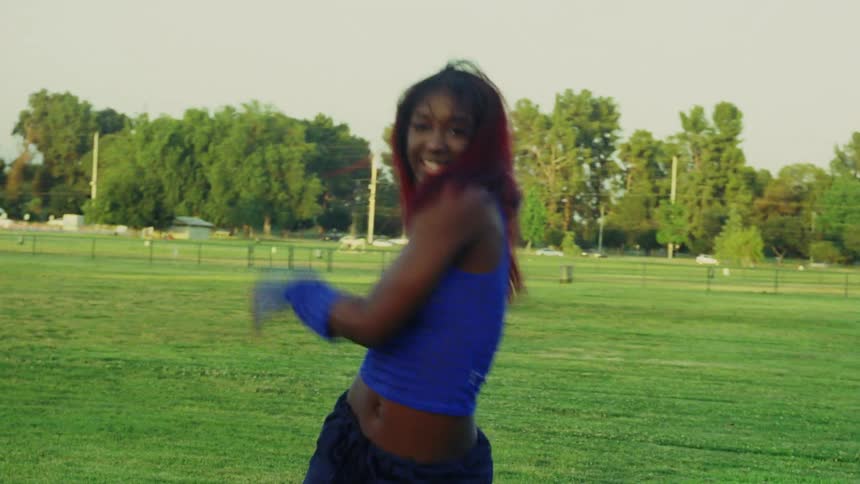 Woman with red hair blue top and sports pants dances on lawn in public park