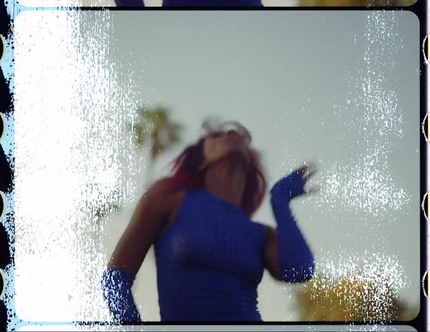 A woman looks into the camera while dancing outdoors during the day