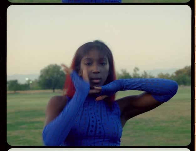 Black woman dances in a field while wearing long blue gloves and a matching blue top